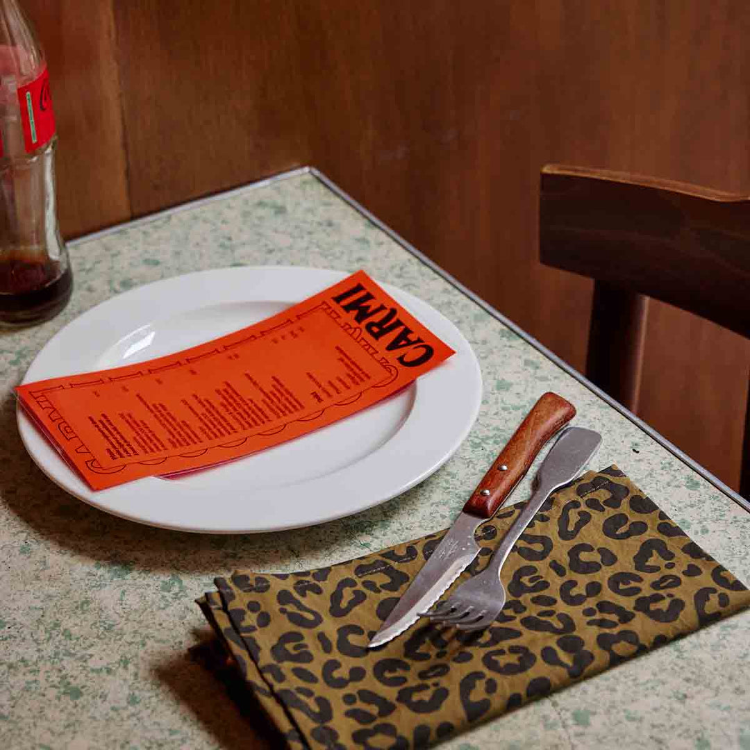 Table setting featuring leopard olive napkin, white plate, and orange menu, creating a chic dining atmosphere.