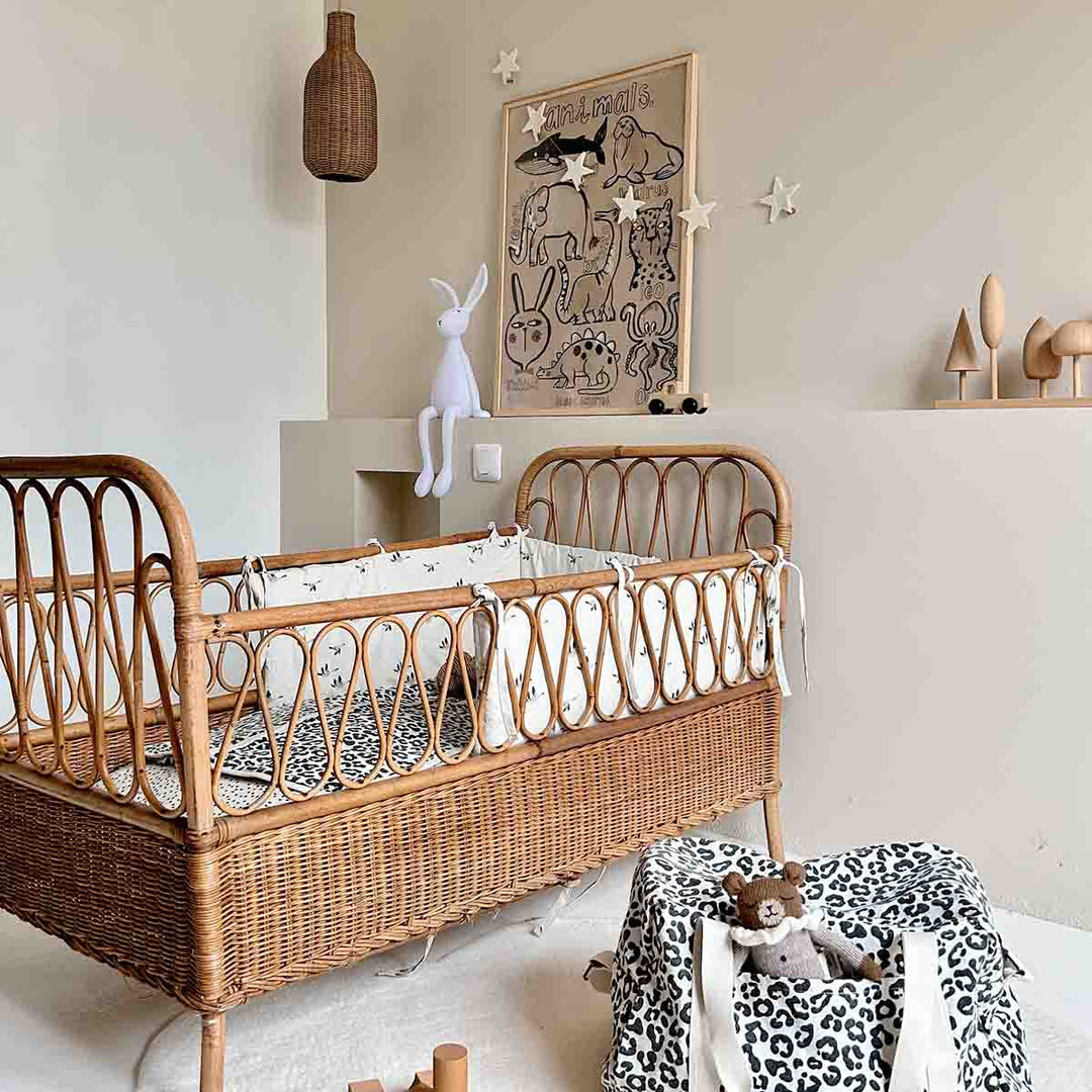Cozy nursery featuring a rattan crib, decorative wall art, and leopard print tote bag for practical storage.