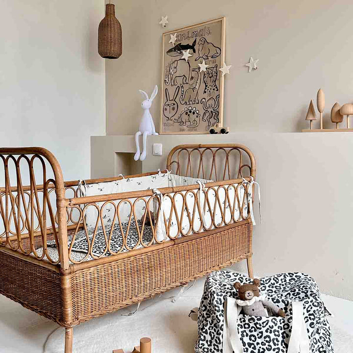 Cozy nursery featuring a rattan crib, decorative wall art, and leopard print tote bag for practical storage.