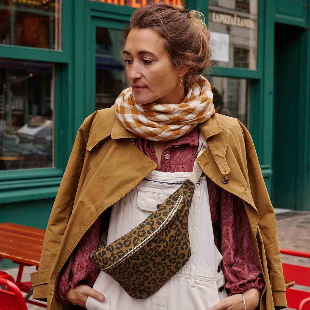 Woman wearing BUM BAG GRAOU OLIVE in leopard print, styled with a brown coat and plaid scarf, showcasing hands-free fashion.