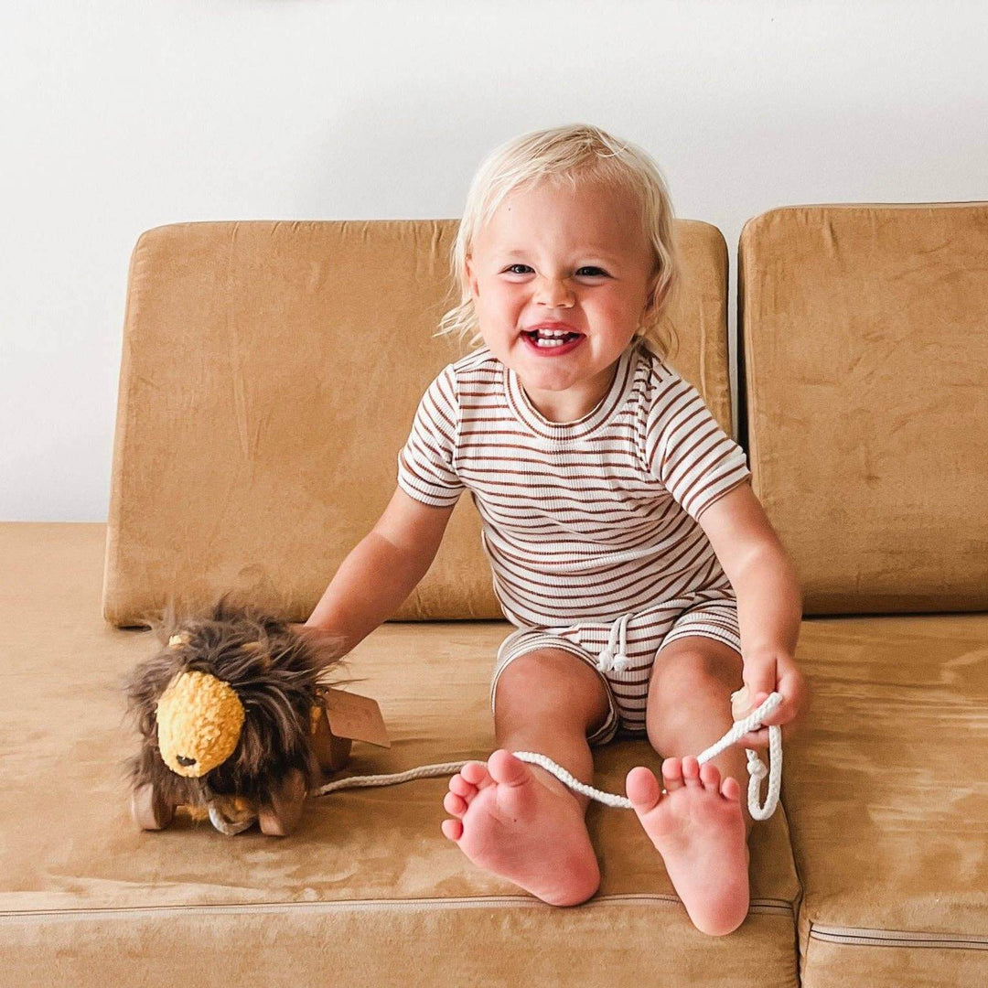 Child playing with LEO toy lion on a couch, encouraging movement and exploration with this fun kids' toy.