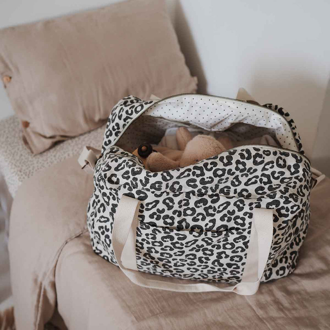 Tote bag in leopard print fabric with teddy bear inside, placed on a bed.