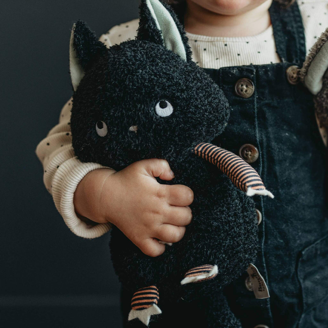 Child holding Boo Boo Kitty cat stuffed animal with soft black fur, orange and black striped arms and legs, and glow in the dark ears and eyes