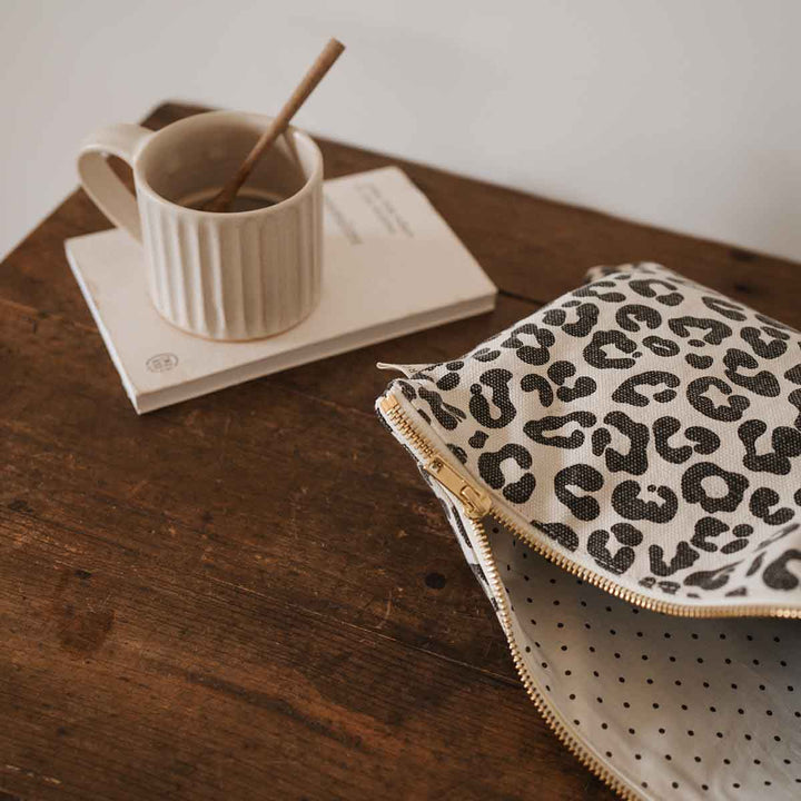 Lili Flat Pouch in leopard greige print with a washed effect, placed next to a cup on a wooden table.