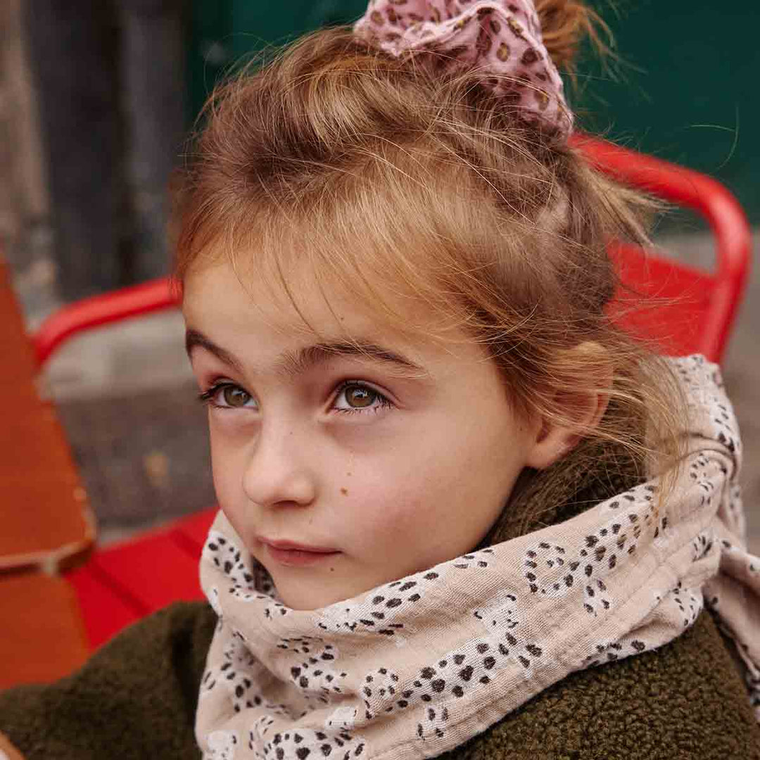 Young girl with a scrunchie wearing a stylish spotted scarf, sitting outdoors, showcasing cozy winter fashion.
