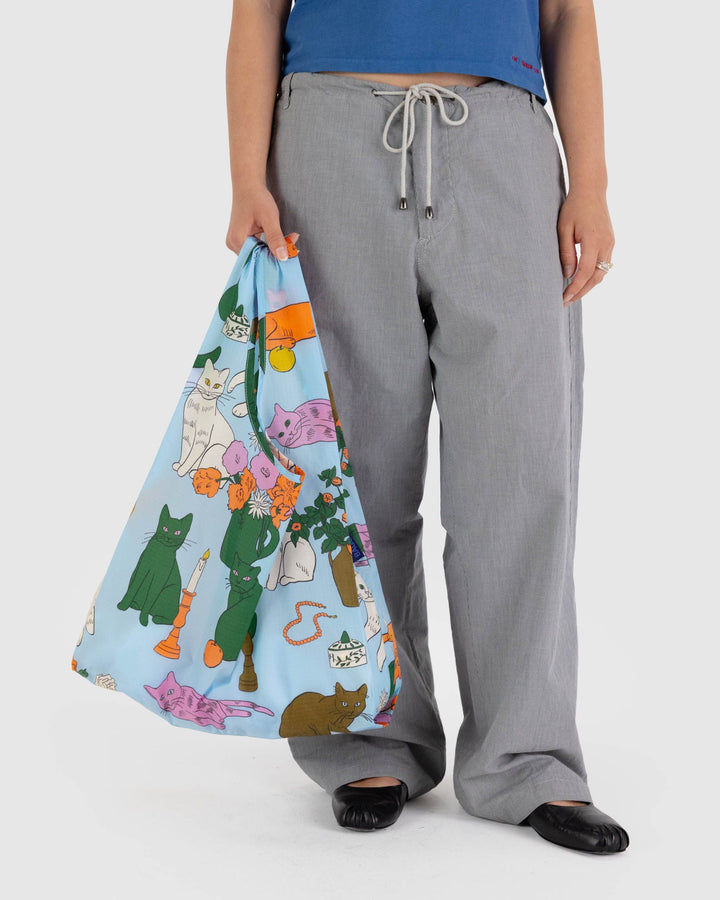 Person holding a Standard Baggu reusable bag with a colorful cat print design, ideal for carrying groceries or other items comfortably.