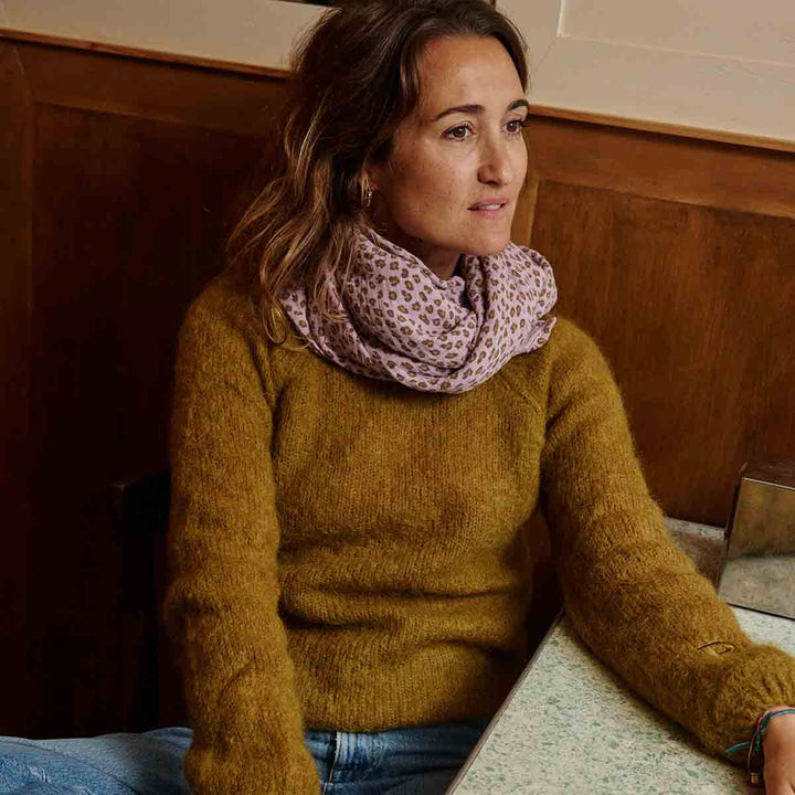 Woman wearing a lilac leopard print scarf with a mustard sweater, sitting at a cafe table.