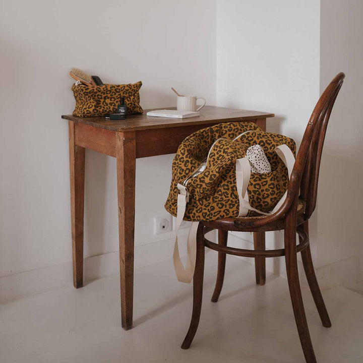 Stylish leopard print tote bag and pouch on wooden table with coffee and chair, perfect for daily use.
