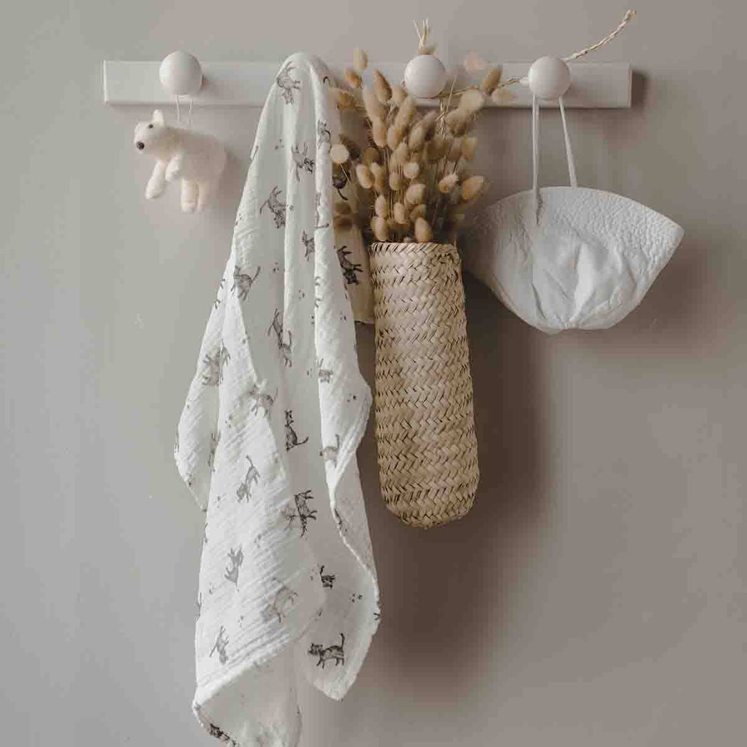Bianca swaddle in ecru with cat print, hanging decor with dried flowers and baby items.