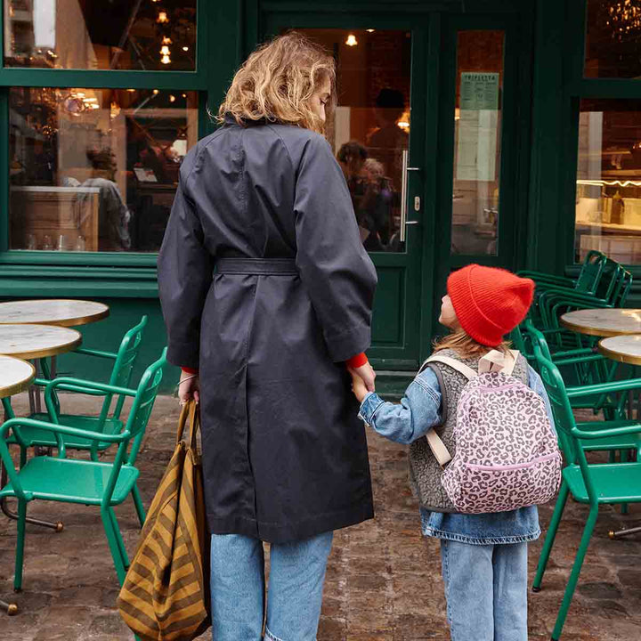A mother and daughter holding hands outside a café, the girl wearing a pink backpack with a leopard print.