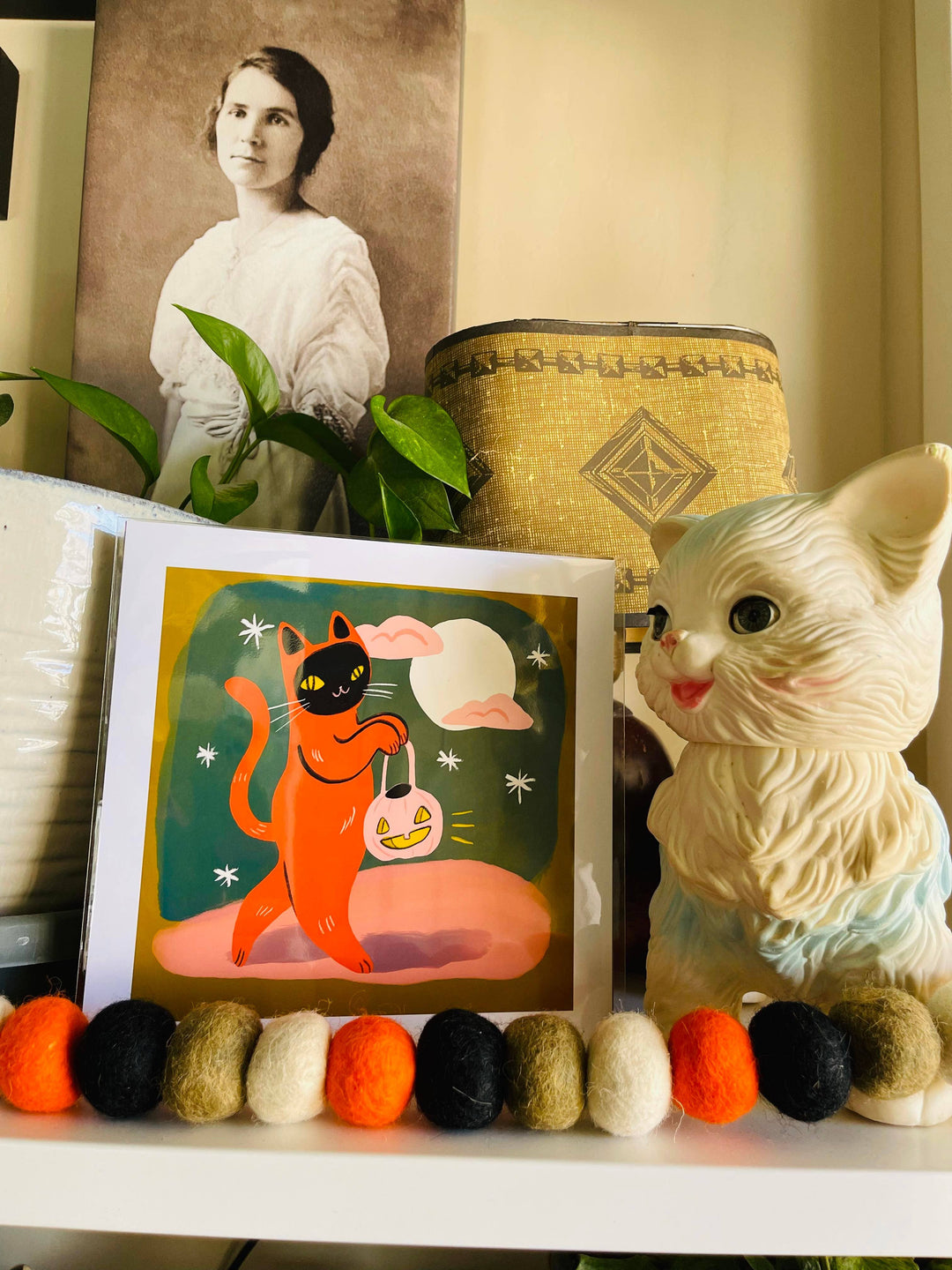 Trick or Treat Orange Cat Print displayed on a shelf with vintage items and cat-themed decorations, perfect for cat art lovers.