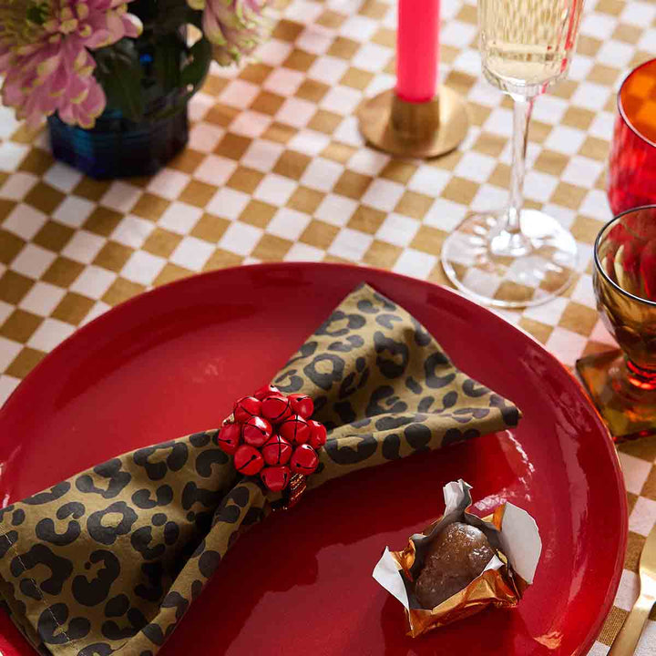 Leopard olive napkin Laurene with red embellishment on a red plate, enhancing chic table decor.