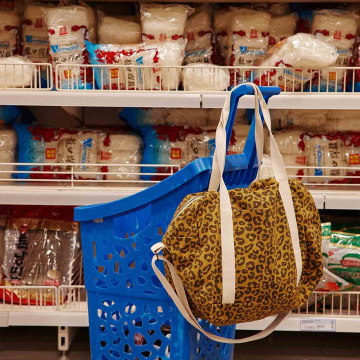 Leopard caramel tote bag hanging on a blue shopping cart in a grocery store aisle.