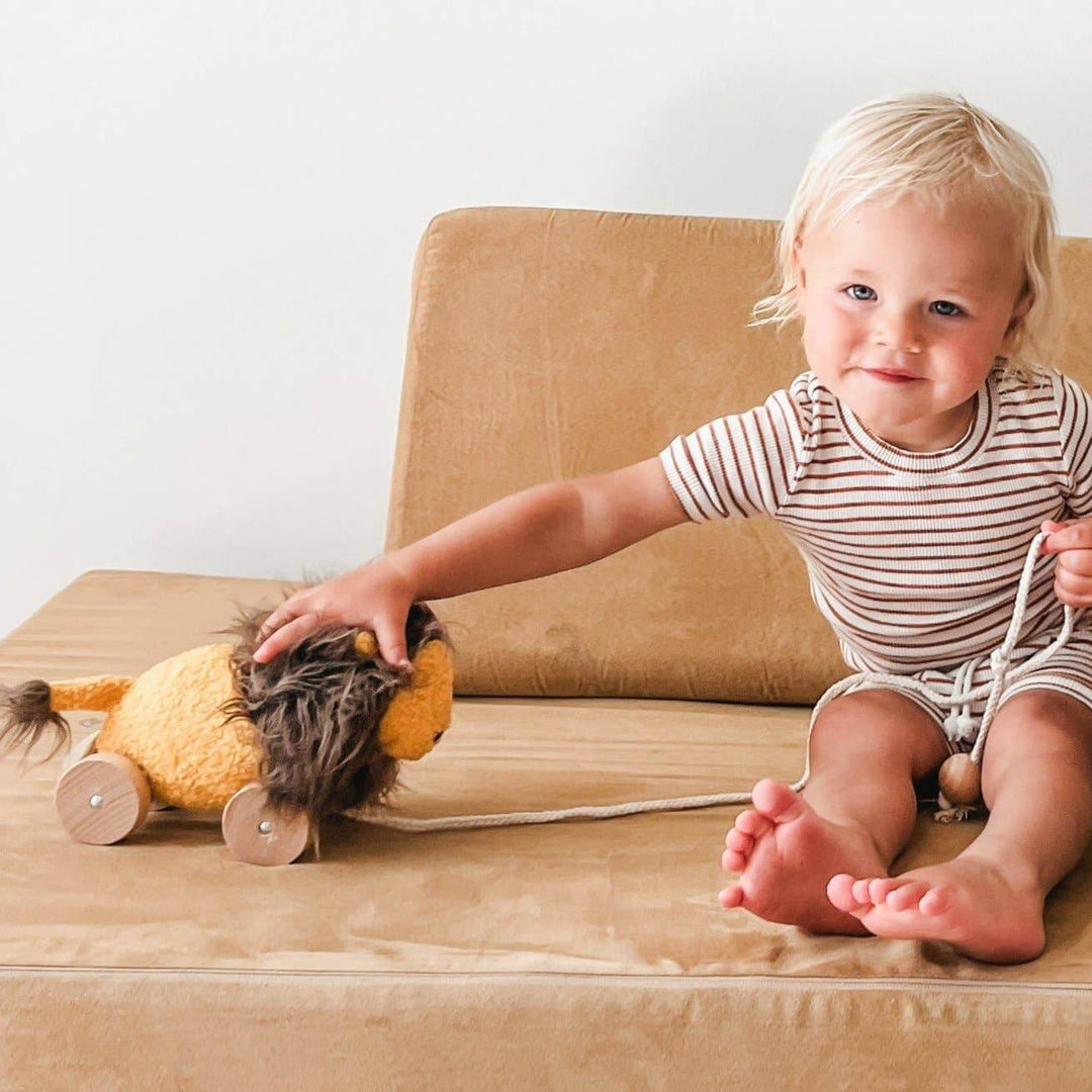 Child playing with LEO toy lion on a sofa, promoting active play and learning, ideal toys for kids.