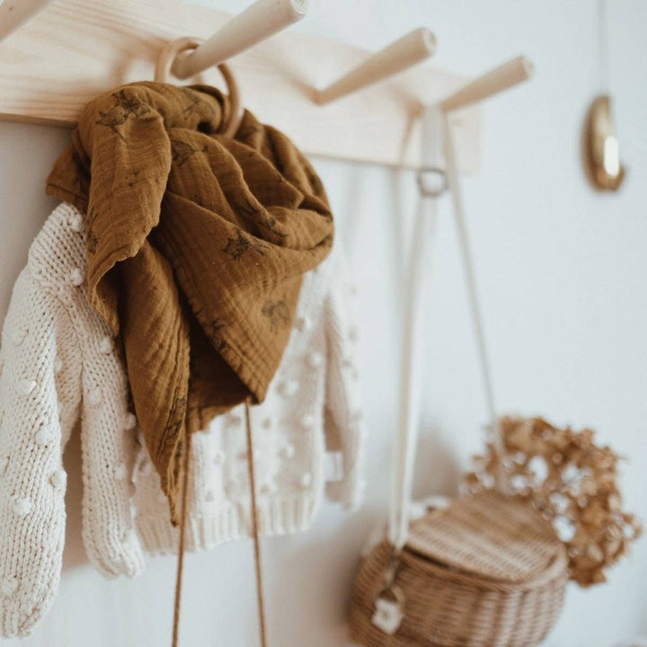 Bianca Swaddle in cumin cat print displayed with a knit sweater and bag on a wooden wall hook.
