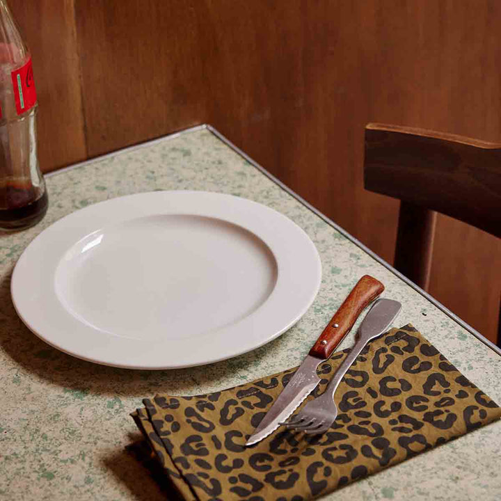 Stylish Laurene leopard olive napkin featuring 100% cotton material on a dining table with a plate and cutlery.