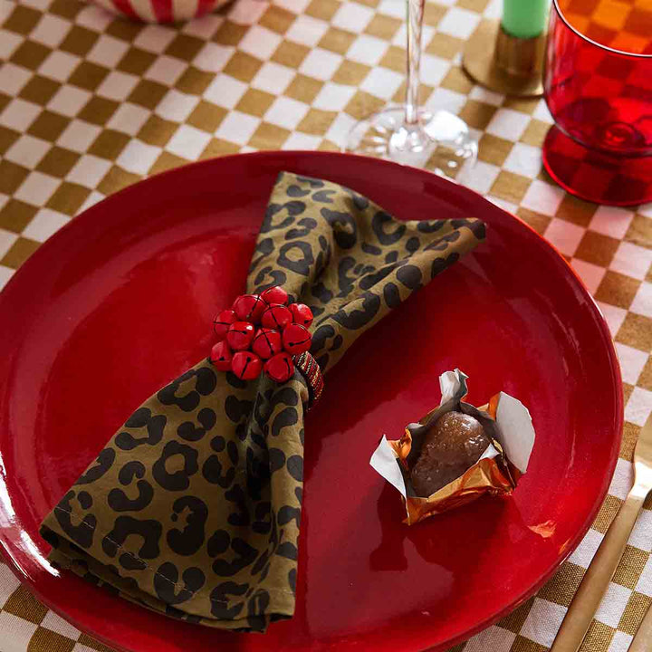 Elegant leopard olive napkin styled on a red plate, accented with a decorative ring and a chocolate treat.