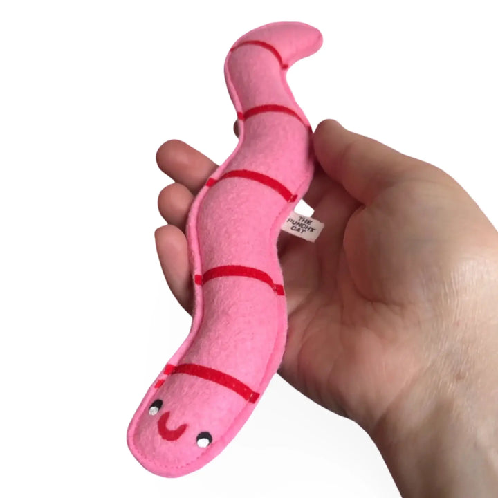 Hand holding a pink catnip worm toy with a smiley face and red markings, perfect for playful cats.
