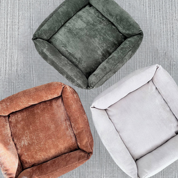 Handmade corduroy pet beds in dark green, brown, and beige, displayed on a gray textured surface. Perfect for stylish and cozy interiors.