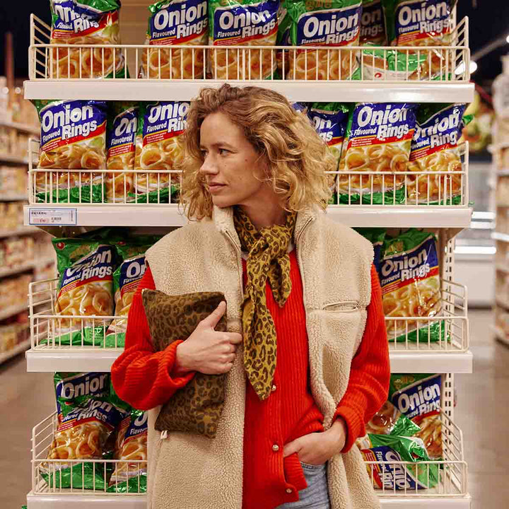 Woman in a grocery store holding a leopard olive flat pouch, standing in front of onion rings display.