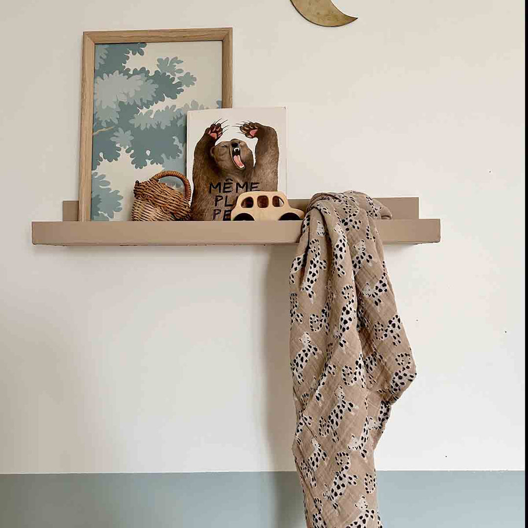 Bianca Swaddle in baby leo print displayed on a shelf with decorative items, symbolizing versatility as a blanket or burp cloth.