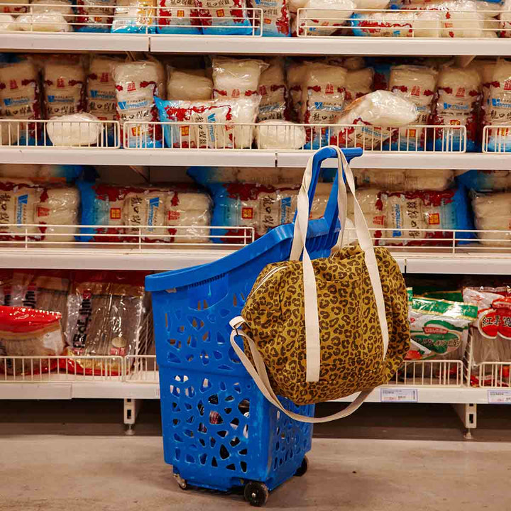 Leopard caramel print tote bag hanging on a blue shopping cart in a grocery aisle with rice bags.