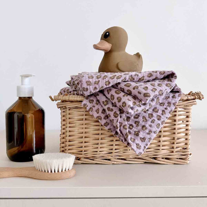 Bianca Swaddle in lilac leopard print displayed in a basket with a duck, bath brush, and soap bottle.