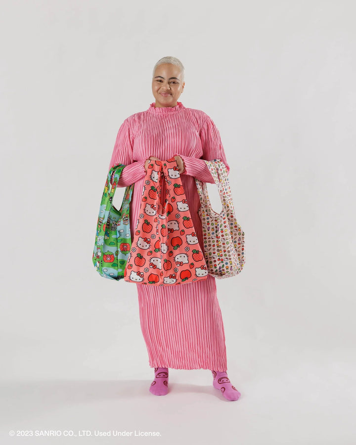 Person holding three unique Hello Kitty and Friends Baggu reusable bags in a pink outfit, showcasing their design and functionality.