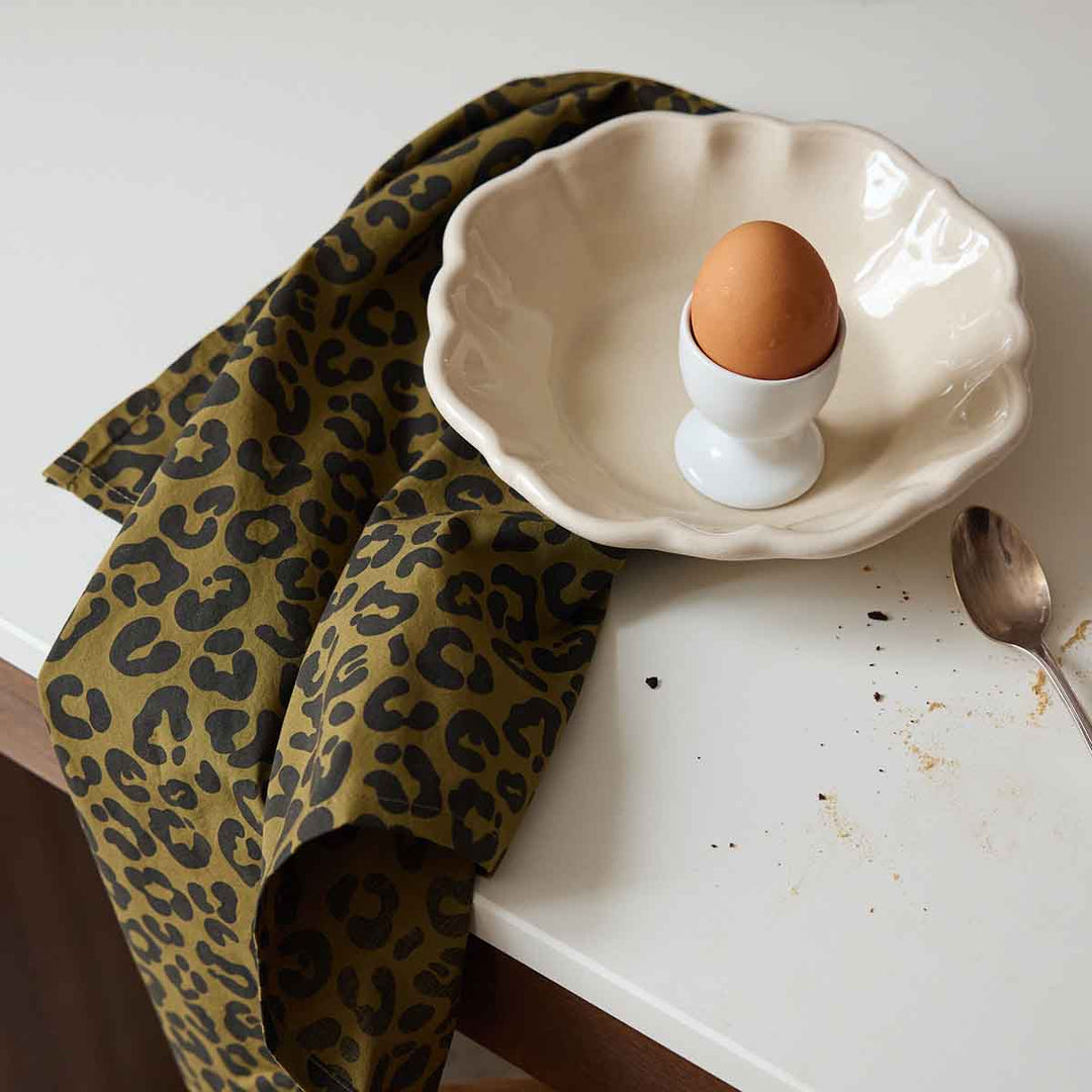 Chic leopard olive napkin on kitchen table, with egg in a dish, enhancing home decor.