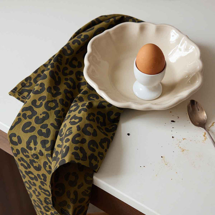 Chic leopard olive napkin on kitchen table, with egg in a dish, enhancing home decor.