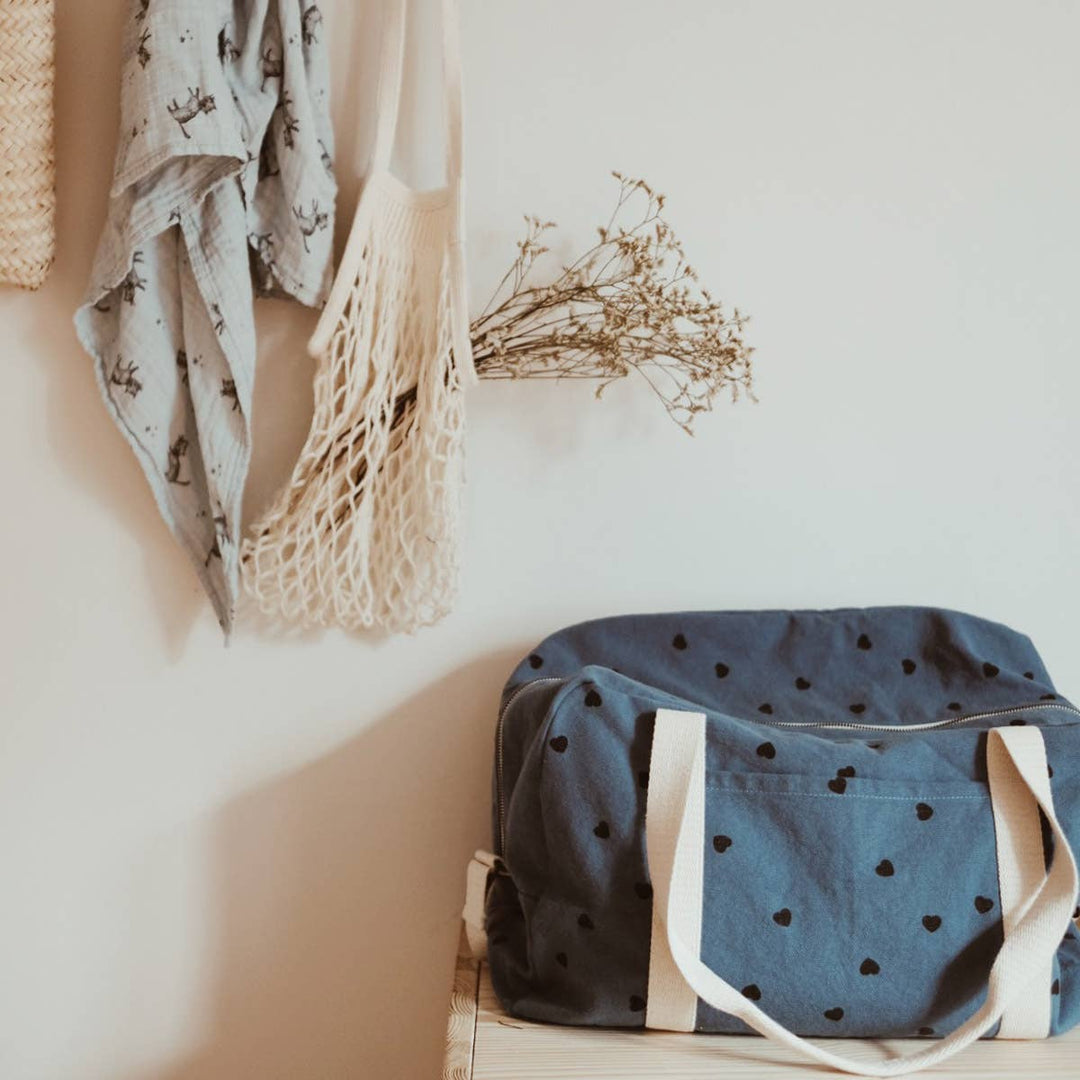 Stylish blue tote bag with heart print placed against a wall, ideal for shopping or everyday use.