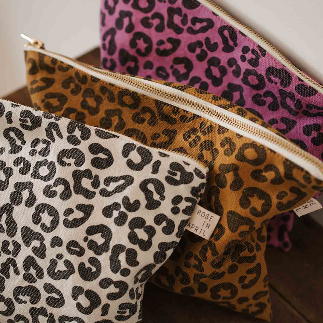 Leopard print flat pouches in caramel, white, and purple on a wooden surface, perfect for toiletries or makeup.