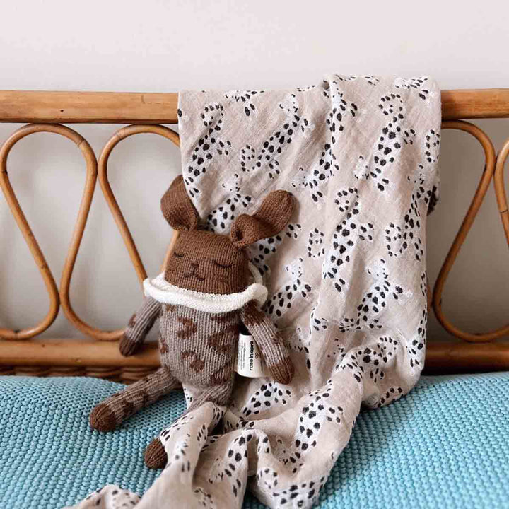 Bianca swaddle in baby leo print draped over a crib, with a playful stuffed bunny toy beside it.