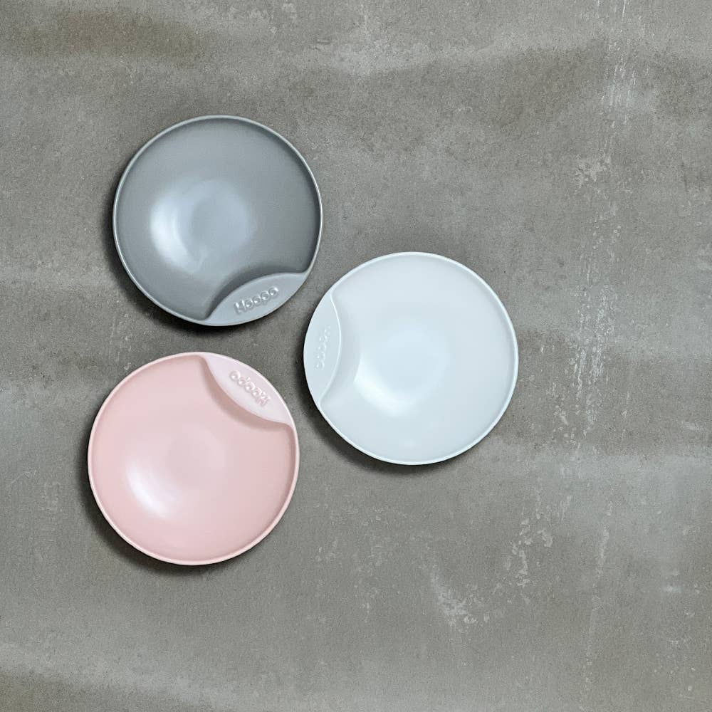 Three cat plate bowls in grey, white, and pink on a grey surface.