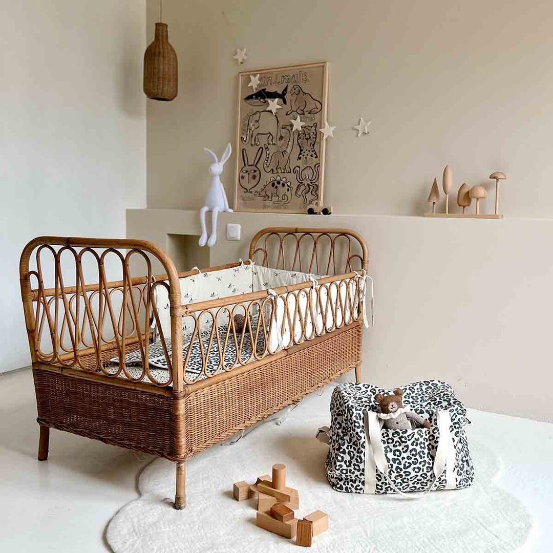 Cozy nursery scene featuring a rattan crib and leopard print tote bag with toys on the floor.