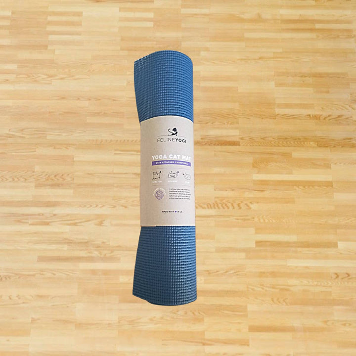 Slate Blue Yoga Cat Mat on a wooden floor, folded and wrapped with a label showing cat scratcher, toy, and lounger features.