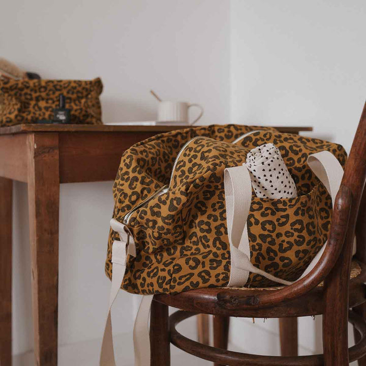 Leopard caramel print tote bag by Raphael Graou on a wooden chair, showcasing its practical design and spacious pockets.