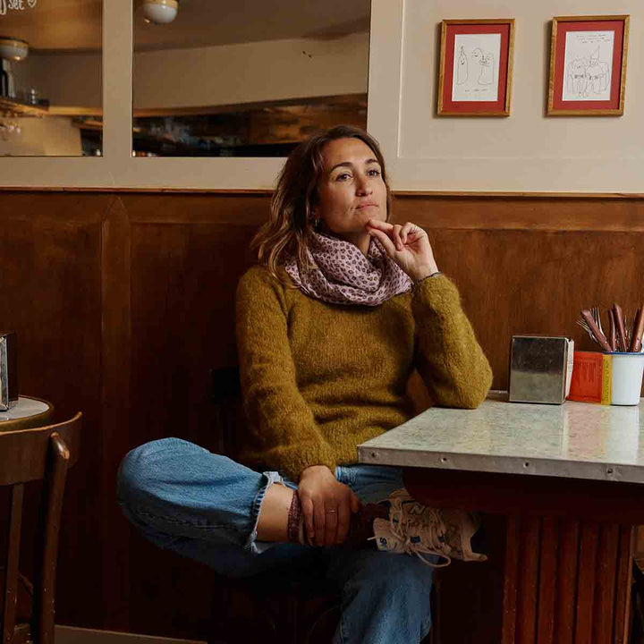 Stylish woman wearing a yellow sweater and leopard print scarf, seated at a café table.