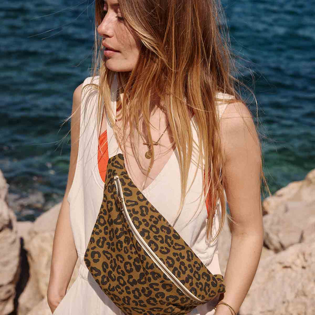 Model wearing a leopard olive print bum bag against a seaside background, showcasing a stylish hands-free accessory.