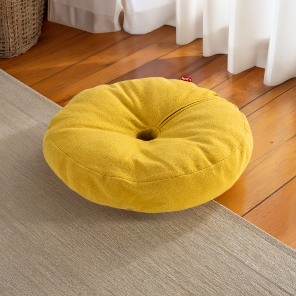 Yellow Donut Cat Bed on wooden floor next to beige carpet, showcasing its soft and cozy design, perfect for any interior.